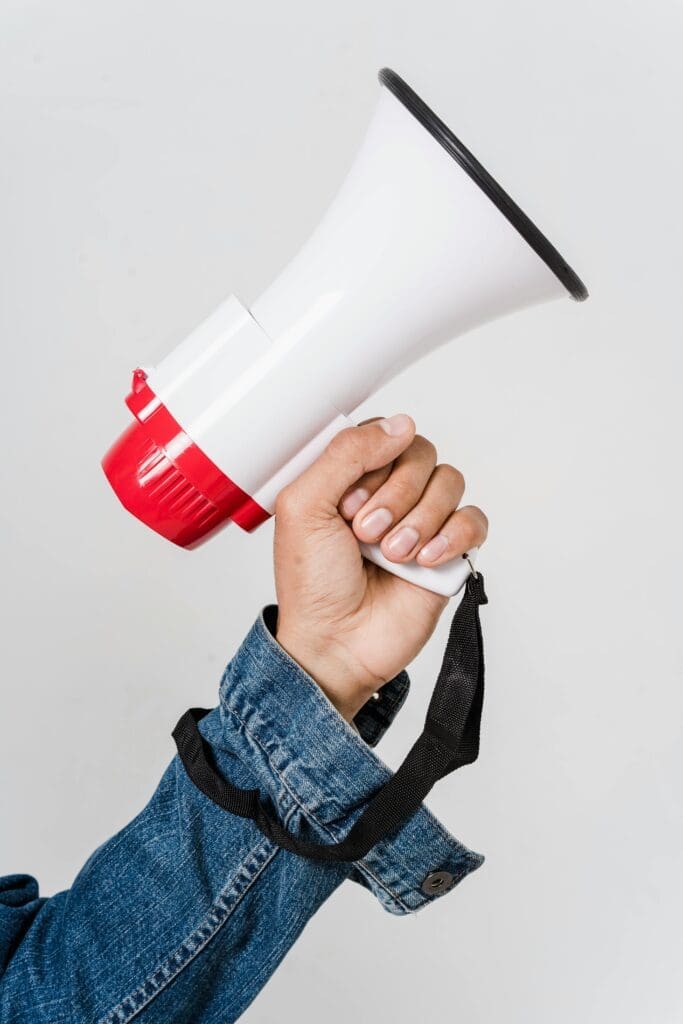 A person in a denim jacket holds a red and white megaphone, emphasizing communication.